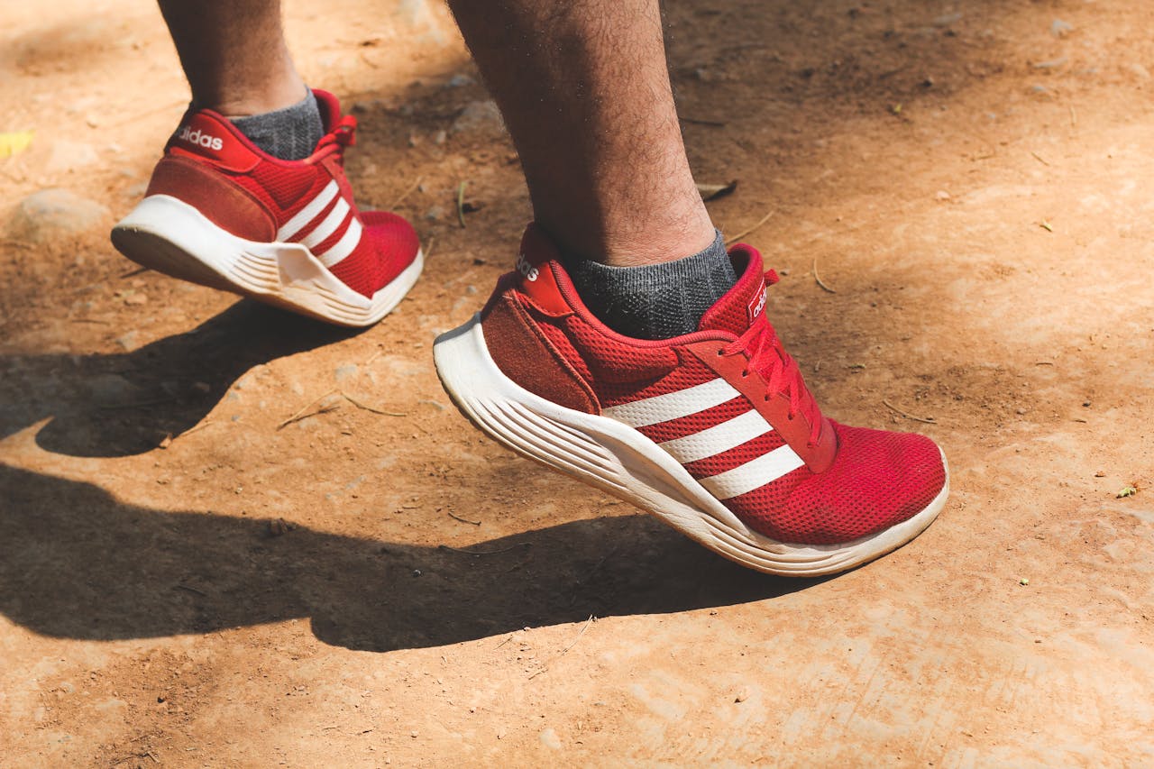 Close-up of red sneakers in motion on a dusty path outdoors.