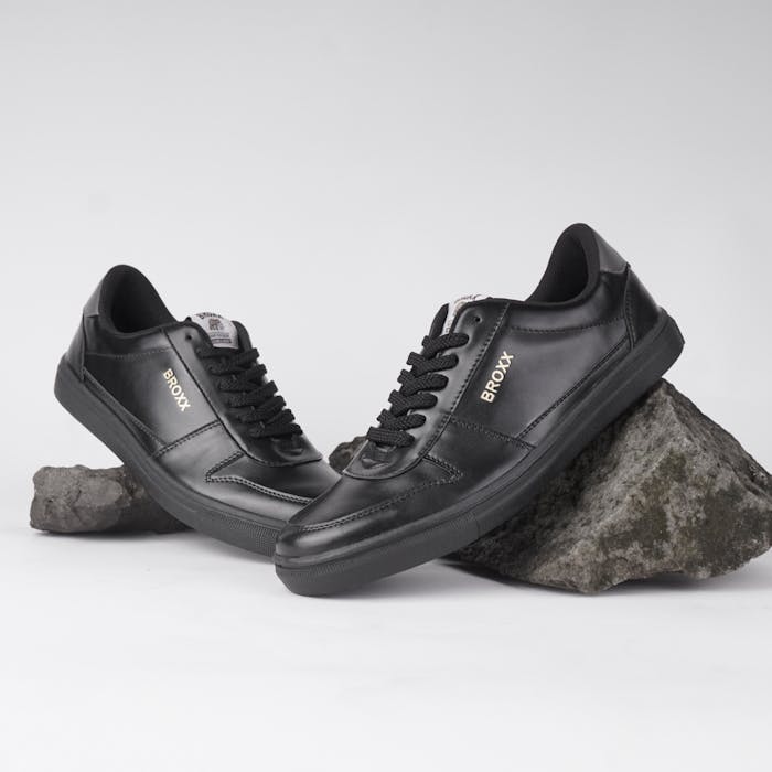 Stylish black sneakers posed elegantly on rocks, showcasing contemporary fashion footwear.