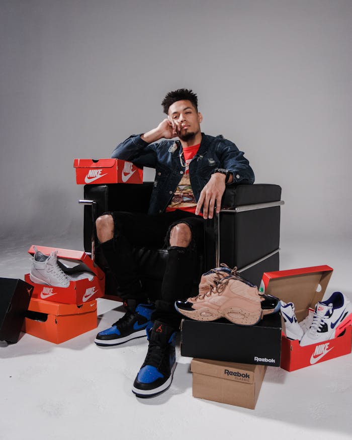Fashionable man posing with a collection of branded shoes in a studio.
